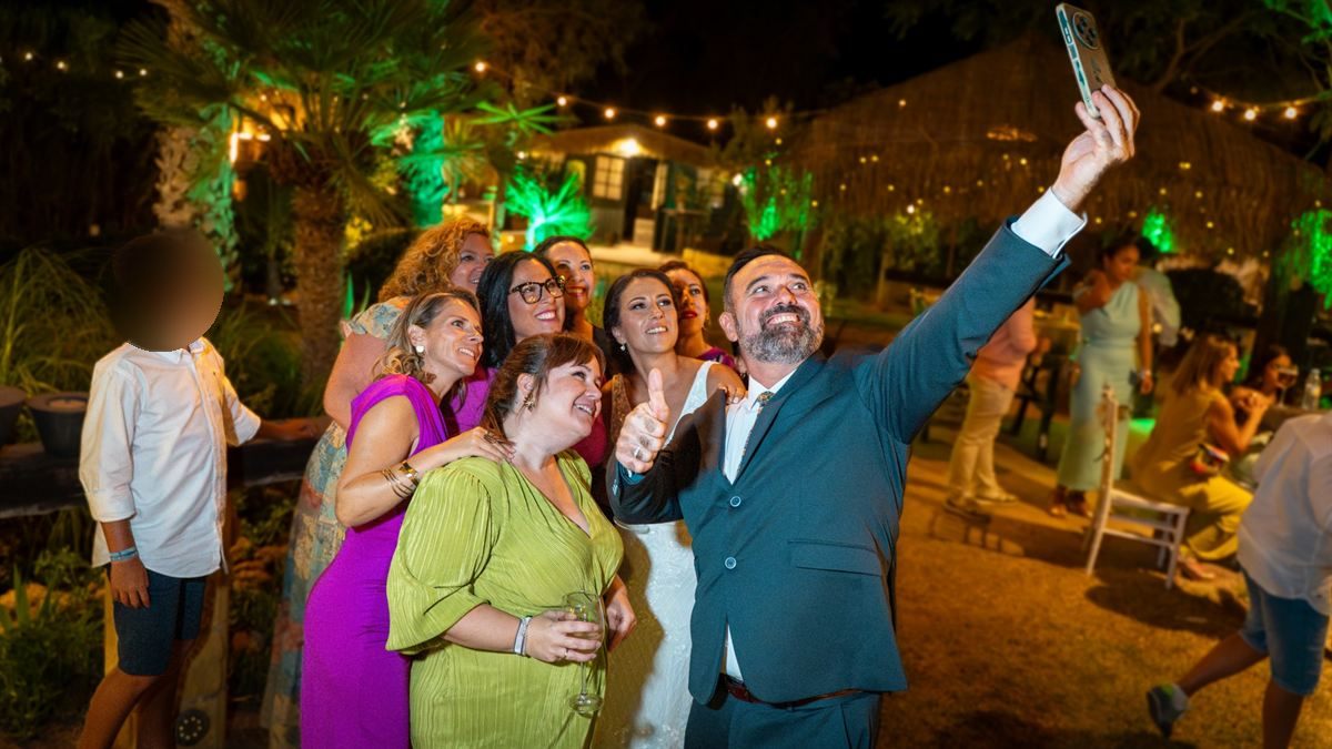 Invitados de boda haciéndose un selfie de noche bajo guirnaldas de luces