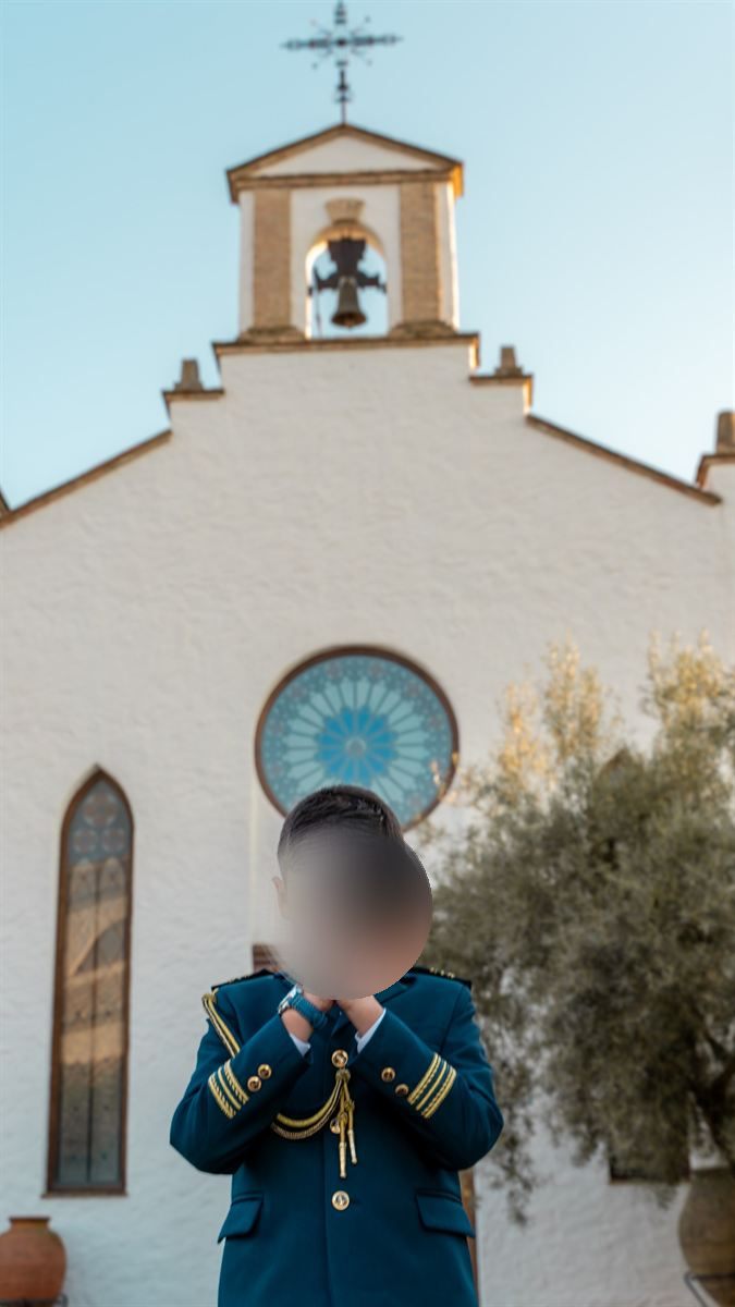 Niño de comunión rezando frente a la fachada blanca de una iglesia andaluza