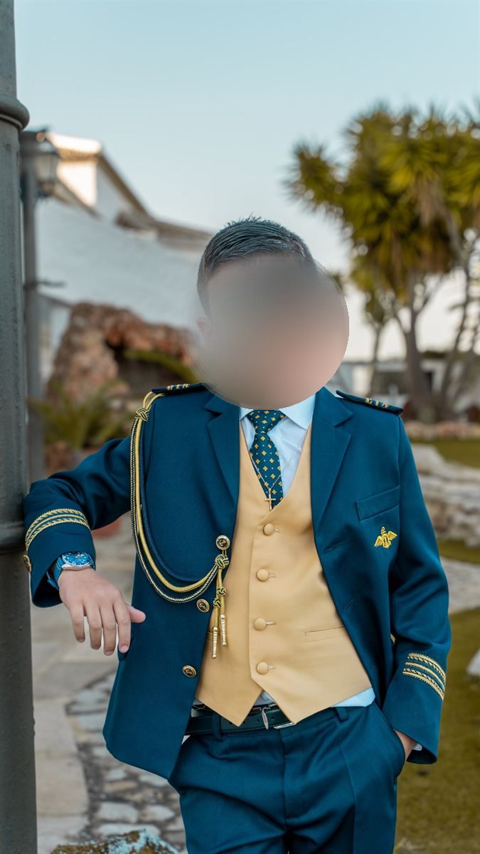 Retrato de niño de comunión con chaleco dorado apoyado en una farola
